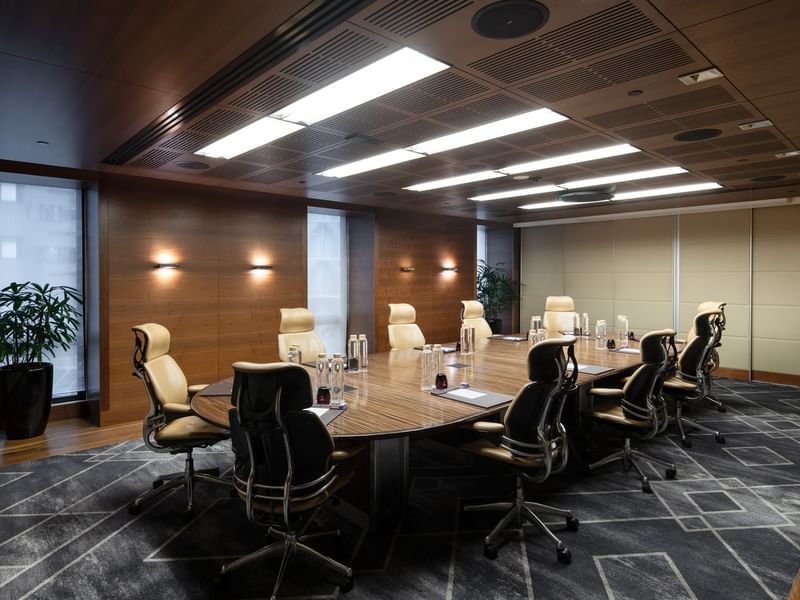Elegant boardroom featuring a polished wooden table, comfortable beige chairs, and a large screen for presentations