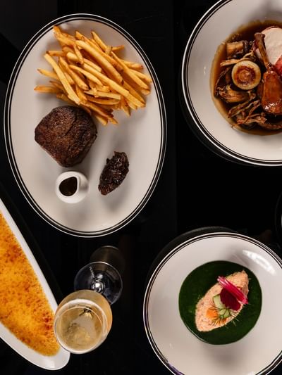 Overhead view of gourmet dishes including steak with fries, seafood, crème brûlée, and plated appetizers at Bistro Suzette