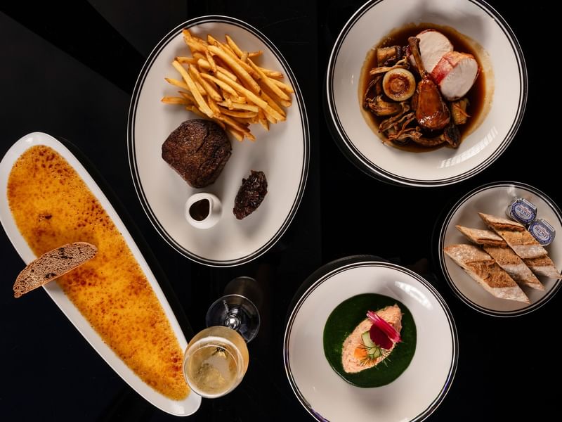 Overhead view of gourmet dishes including steak with fries, seafood, crème brûlée, and plated appetizers at Bistro Suzette