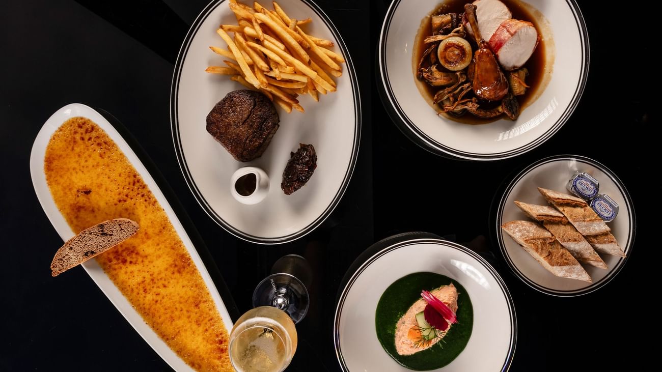 Overhead view of gourmet dishes including steak with fries, seafood, crème brûlée, and plated appetizers at Bistro Suzette