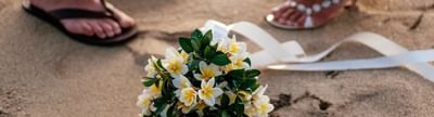 Floral wreath on sand with two people's feet wearing flip-flops in the background at Musket Cove Island Resort & Marina