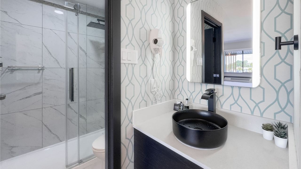 Hotel bathroom with toilet, sink, mirror, shower, towels and soap