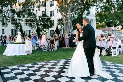 A couple dances on a checkered floor at The White House Hotel, surrounded by guests and glowing outdoor lights