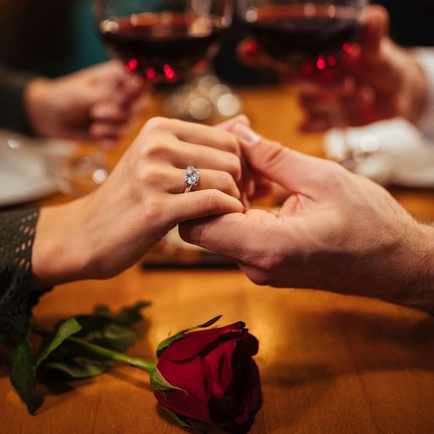 Pareja se toma de la mano junto a un anillo de compromiso con diamante, una rosa roja y vino en Megapolis Hotel Panama