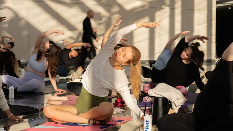 Guests practicing seated side stretches on yoga mats in warm natural sunlight during a wellness class at Hotel X Toronto