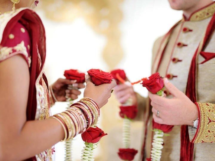 Bride and groom in ornate Indian attire holding red rose garlands during a wedding ceremony at Fiesta Americana Travelty