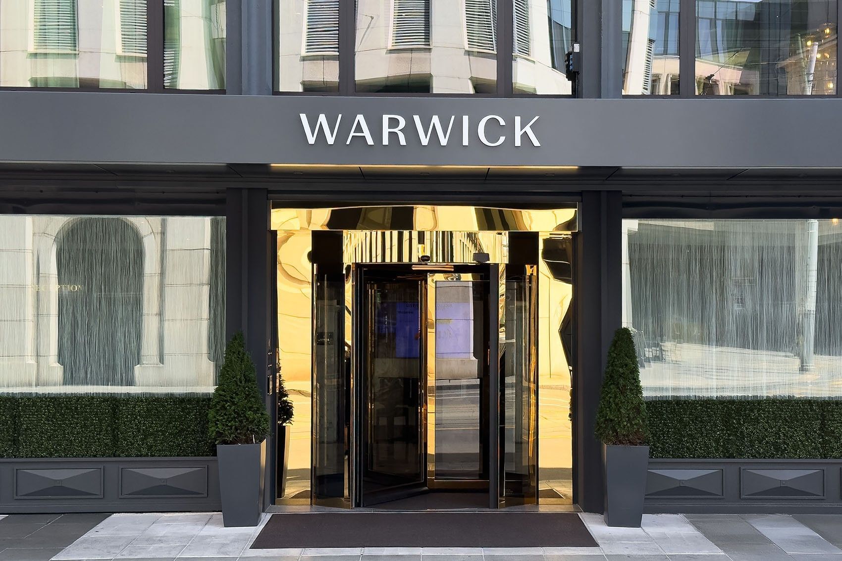 Entrée principale moderne avec porte tournante et enseigne lumineuse au Warwick Geneva Genève