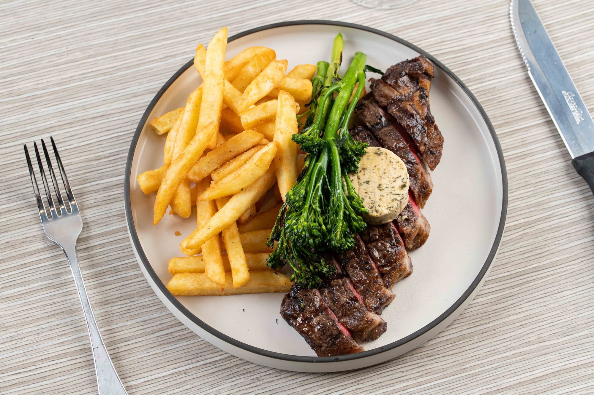 Juicy steak with fries and broccolini, topped with herb butter, served at Ibis Adelaide
