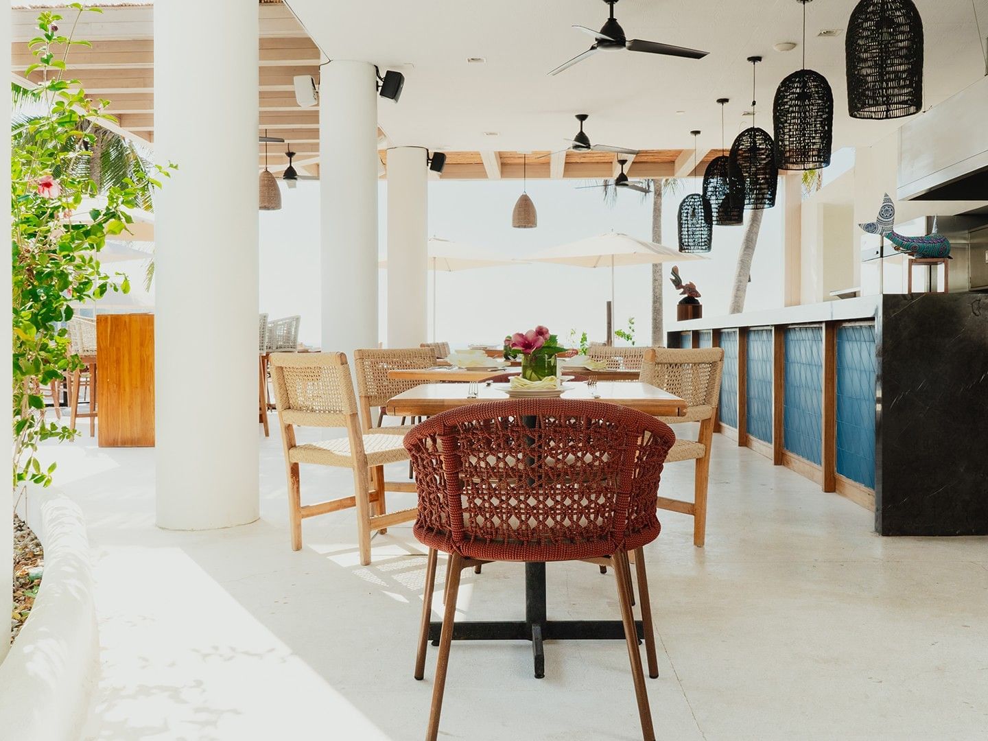 Dining tables and woven chairs arranged in Bel La Grill with lush green plants at Camino Real Zaashila Huatulco