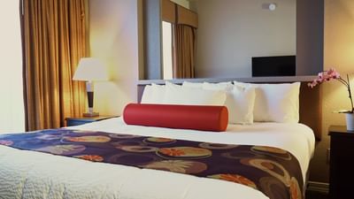 Hotel room with white bedding, red bolster pillow, decorative bed runner, and wall-mounted TV at London Bridge Resort