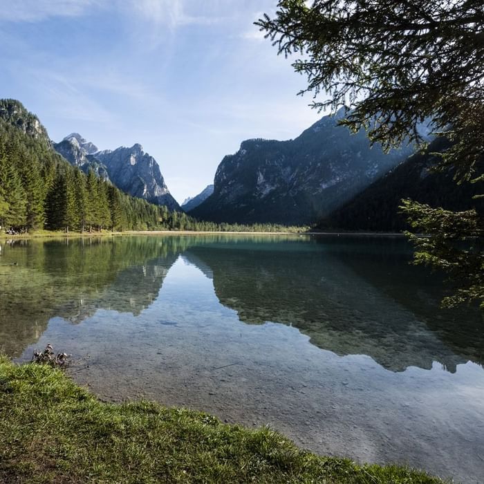 Lago alpino con riflessi di montagne e vegetazione sotto un cielo azzurro.
