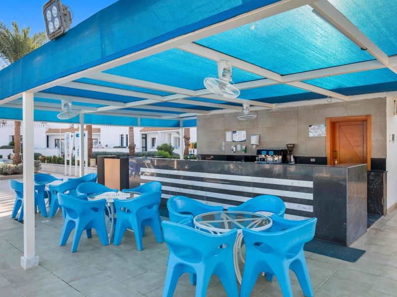 مجموعة من الكراسي والطاولات الزرقاء تحت مظلة زرقاء مع بار في الخلفية.