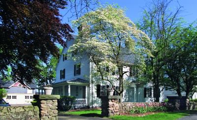 Exterior view of Guest House framed by blooming trees behind a stone wall with flowers at Farmington Inn and Suites