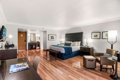 Spacious suite with a king bed beside a lounge chair and ottoman on wooden flooring in the Junior Suite at Miami Lakes Hotel