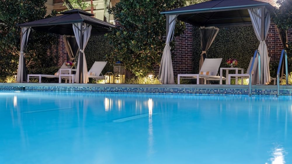 Clear swimming pool with white lounge chairs and decorative gazebos at Warwick Melrose - Dallas.