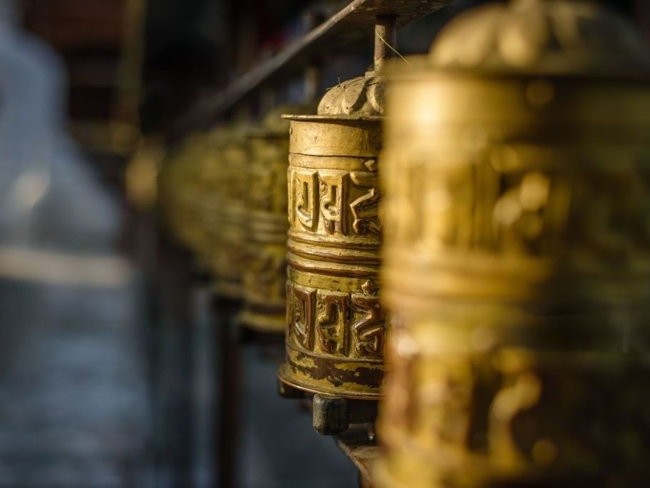 Close-up of lined-up weathered golden prayer wheels, inscribed with symbols near Dwarika's Himalayan Wellbeing