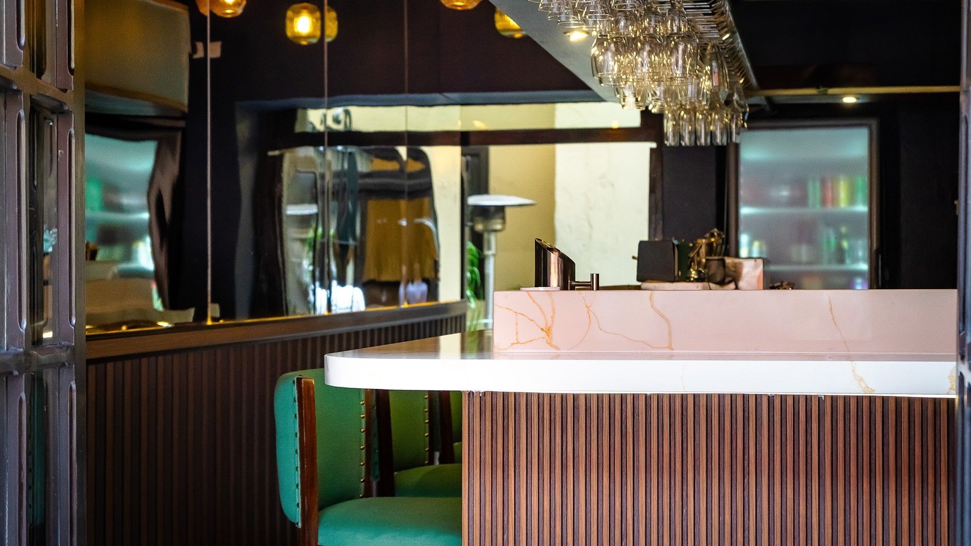 Modern bar interior with a marble counter, green velvet stools, and hanging glassware at Quinta Real Puebla