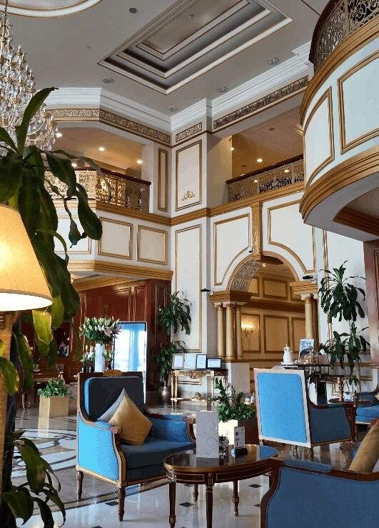 ردهة فندق فخمة بأسقف عالية مزخرفة وأثاث أزرق أنيق ونباتات خضراء في Warwick Doha
