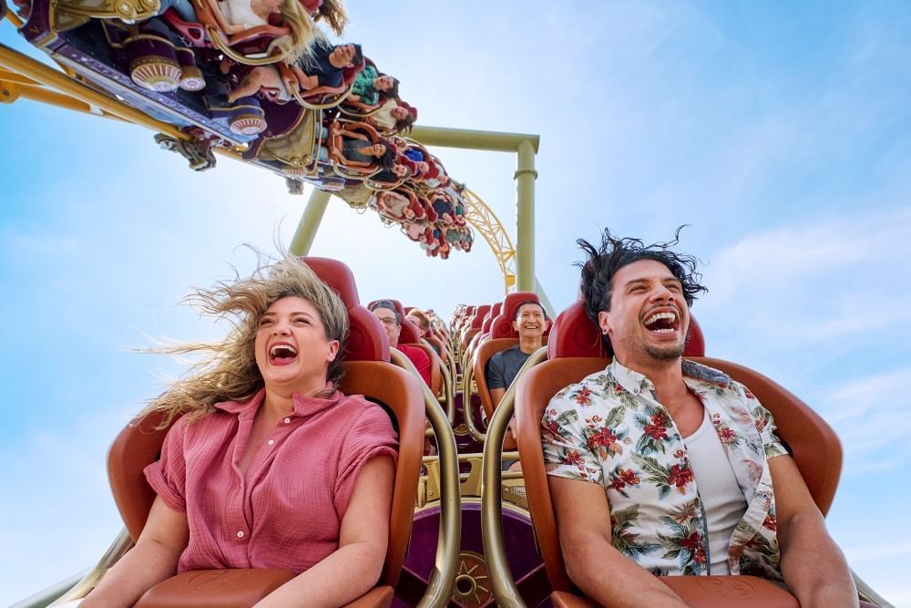 A close up of a man and woman riding a roller coaster with a second track full of riders gliding overhead.