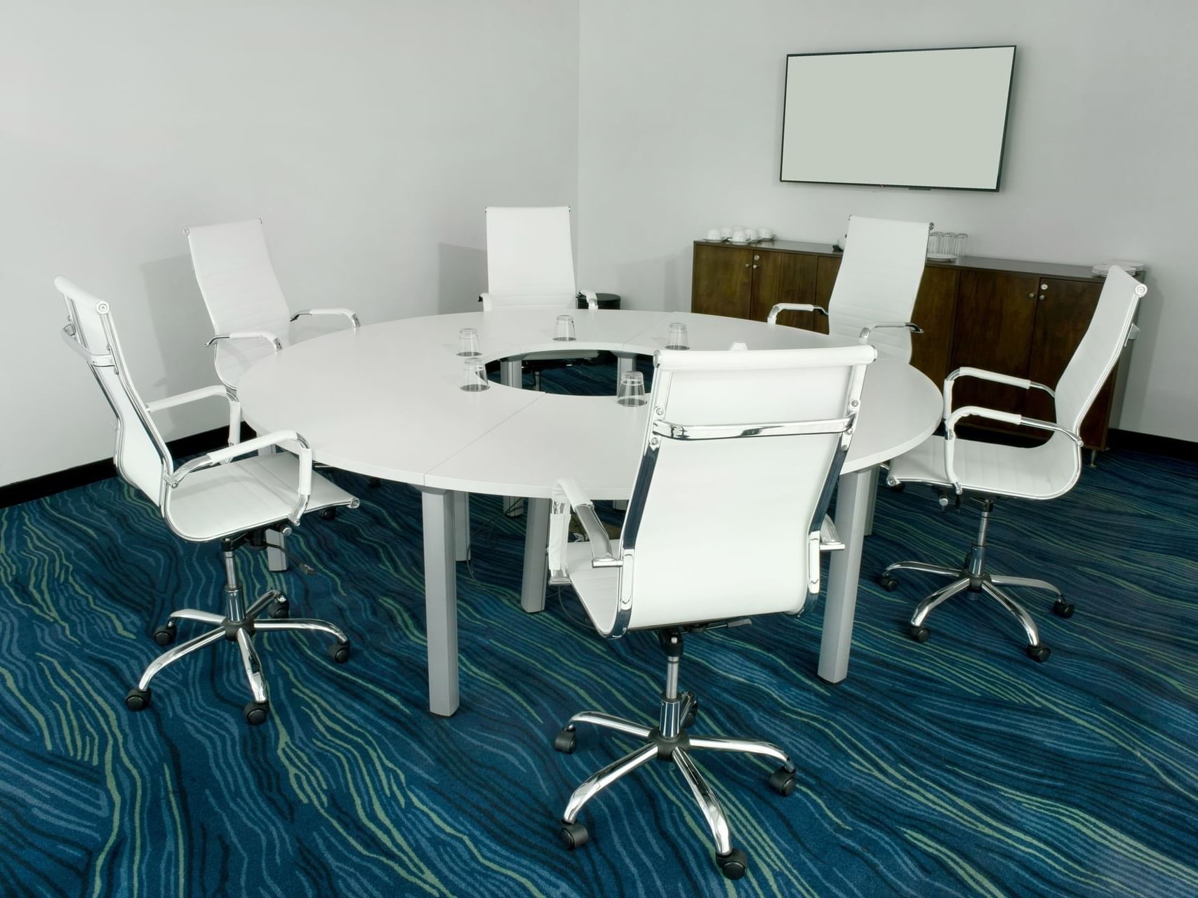 Little Room with circular table, chairs & carpeted floor with a blank wall-mounted screen at D Sabana Hotel