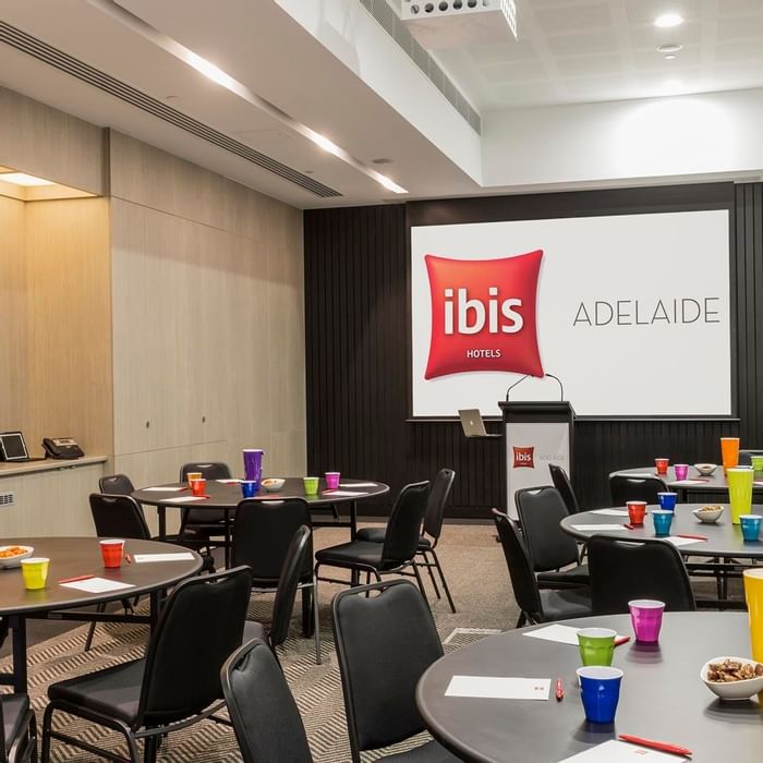 Round tables set up with chairs facing a large projection screen in The Think Tank at Ibis Adelaide