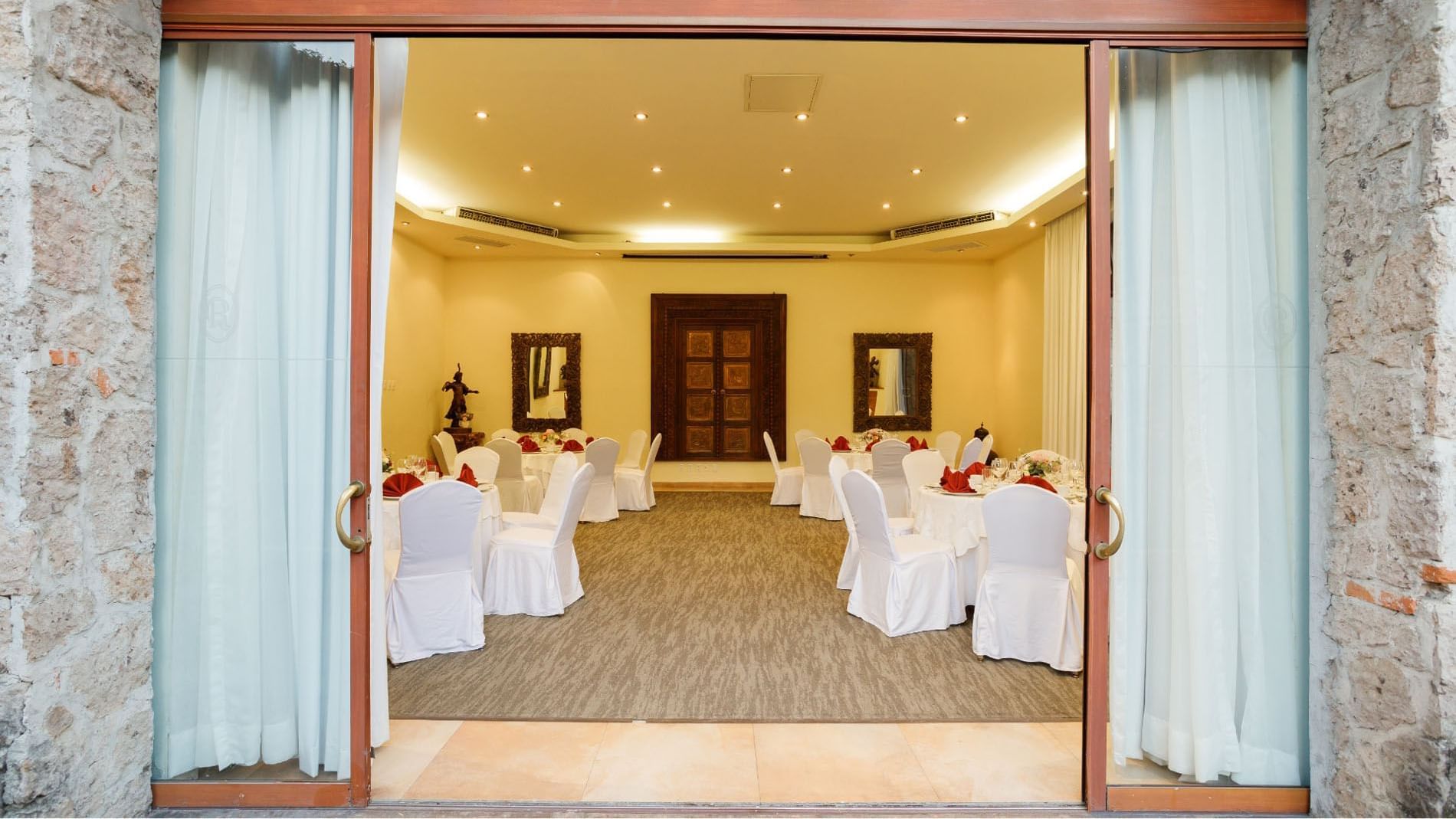 View through open doors into a Salón Cuatro Estaciones event hall with round tables at Quinta Real Guadalajara