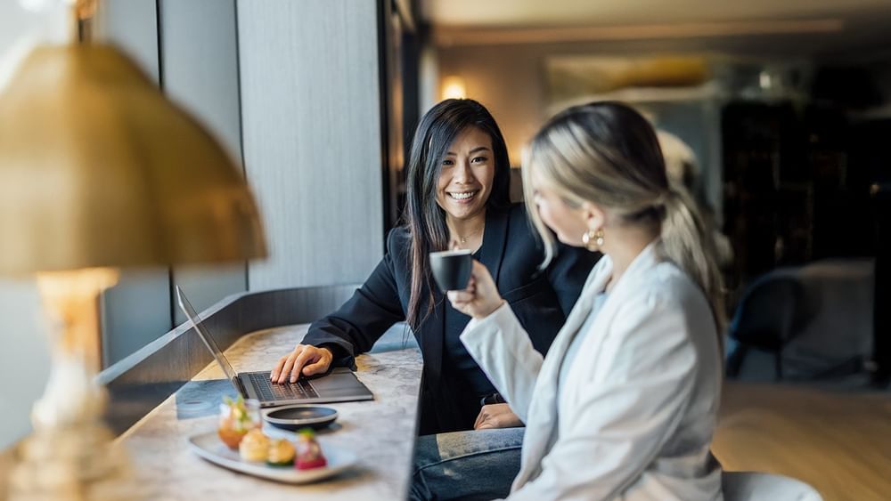 Two guests with a laptop and coffee at a marble desk at Novotel Sydney Olympic Park