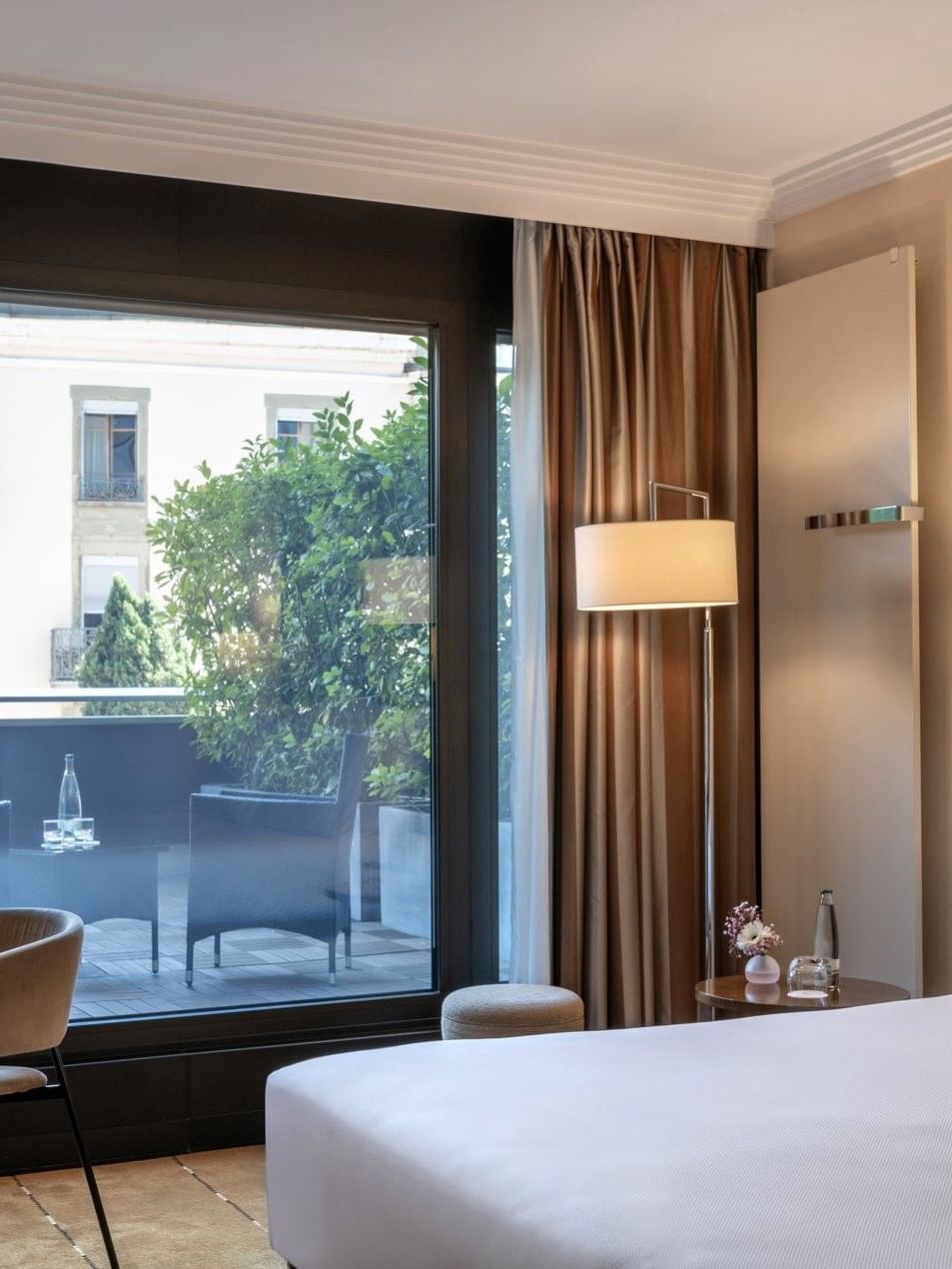 Plush bed by a wooden desk with a lamp, facing a terrace in Deluxe Terrace Room at Warwick Geneva