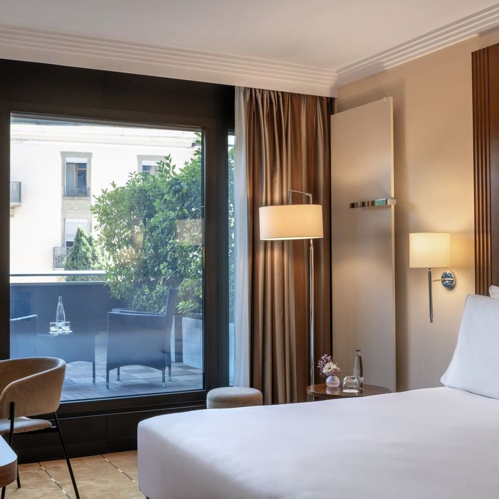 Plush bed by a wooden desk with a lamp, facing a terrace in Deluxe Terrace Room at Warwick Geneva
