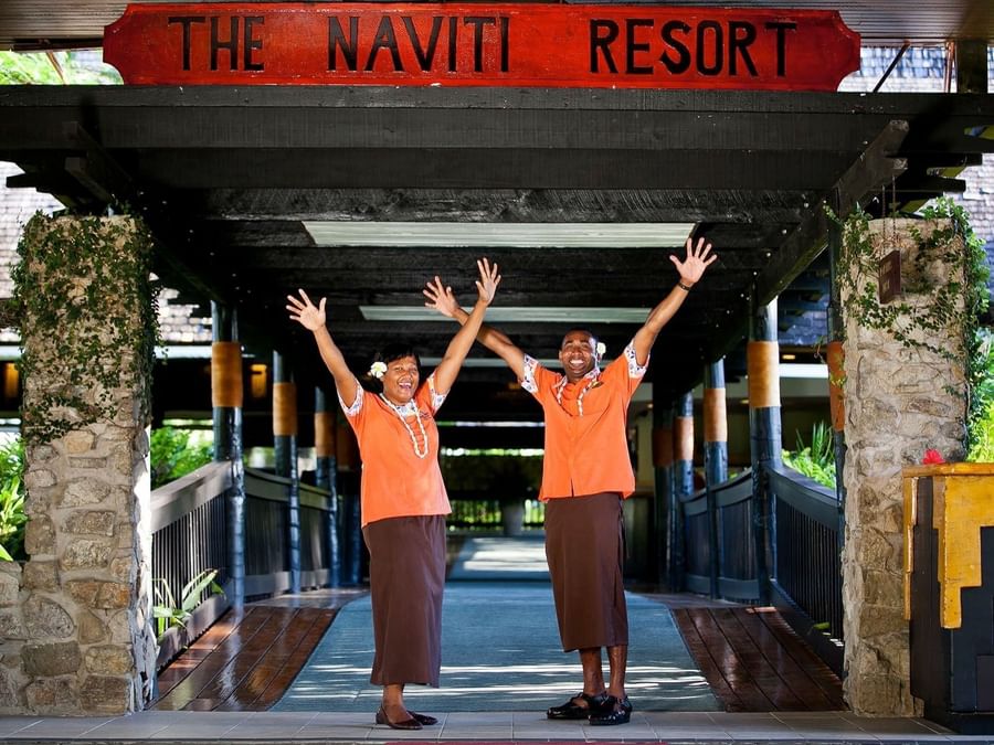Smiling staff by stone pillars under the resort signage near the walkway at The Naviti Resort - Fiji