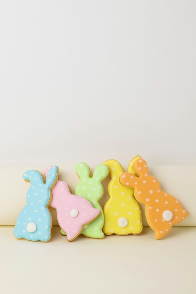 Five rainbow colored bunny sugar cookies with tails against a white background. 