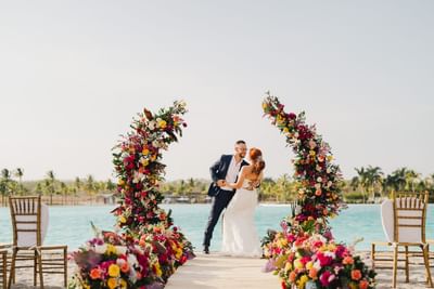 Couple by a floral wedding arch with a sea backdrop at Playa Blanca Beach Resort