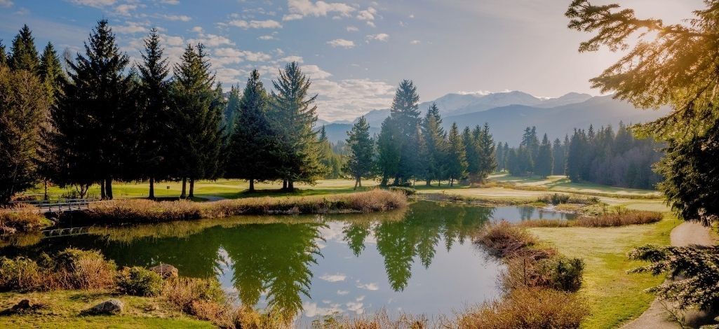 Pond and tree-lined fairways at Whistler Golf Club surrounded by mountain scenery.