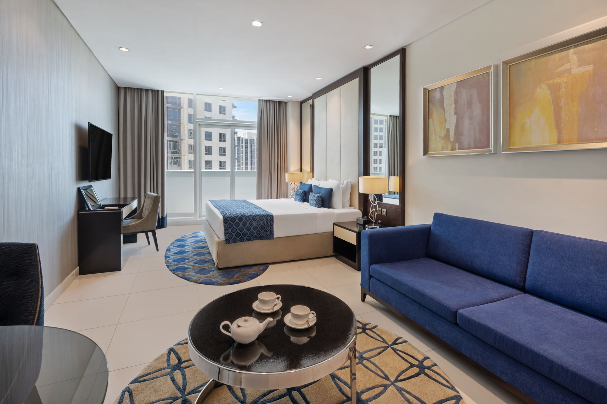Seating area, TV, and work desk by the bed in Deluxe Room at DAMAC Maison Distinction, one of the best hotel rooms in Dubai