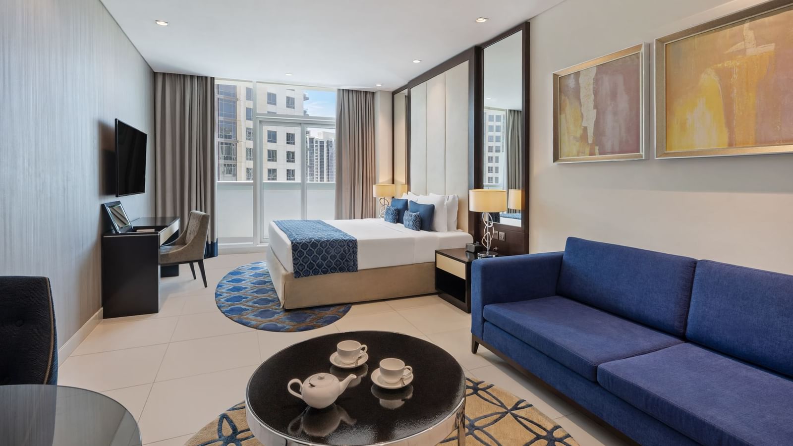 Seating area, TV, and work desk by the bed in Deluxe Room at DAMAC Maison Distinction, one of the best hotel rooms in Dubai