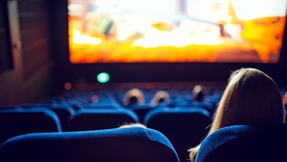 The back of a woman and child sitting in movie theatre seats watching an indoor movie on a big screen.