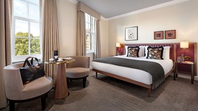 Elegant Collection Superior Room at The May Fair Hotel with a large bed adorned with two beige chairs by a coffee table