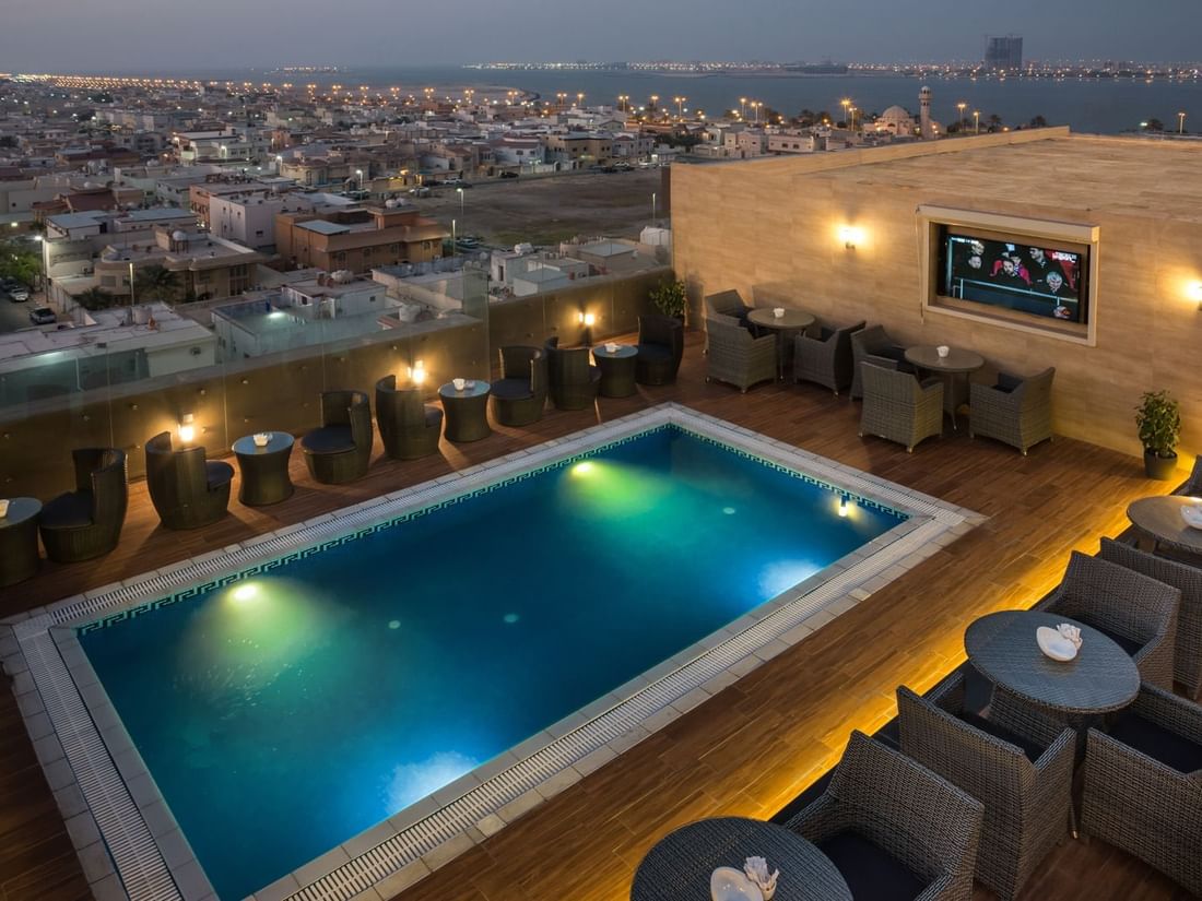 Rooftop pool featuring colorful floats by woven chairs in Sky View Café at Naviti By Warwick Dammam