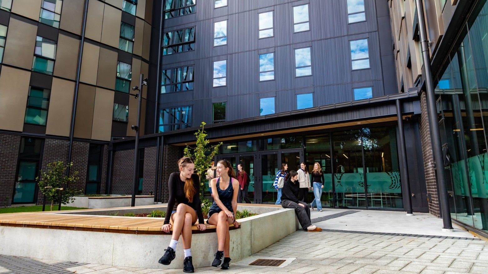 Modern courtyard with students relaxing on concrete benches surrounded by contemporary multi-story buildings at Tupuārangi