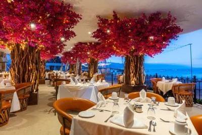 Elegant oceanfront restaurant with illuminated red-flowering trees and white-clothed tables at Playa Los Arcos Puerto Vallarta