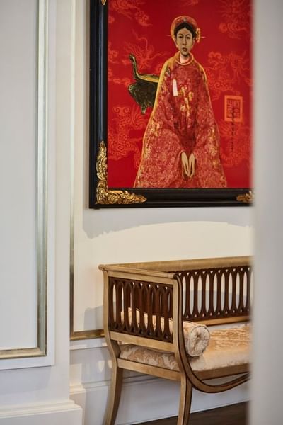 Wooden bench positioned near vibrant red artwork featuring a traditional figure at Park Hyatt Saigon