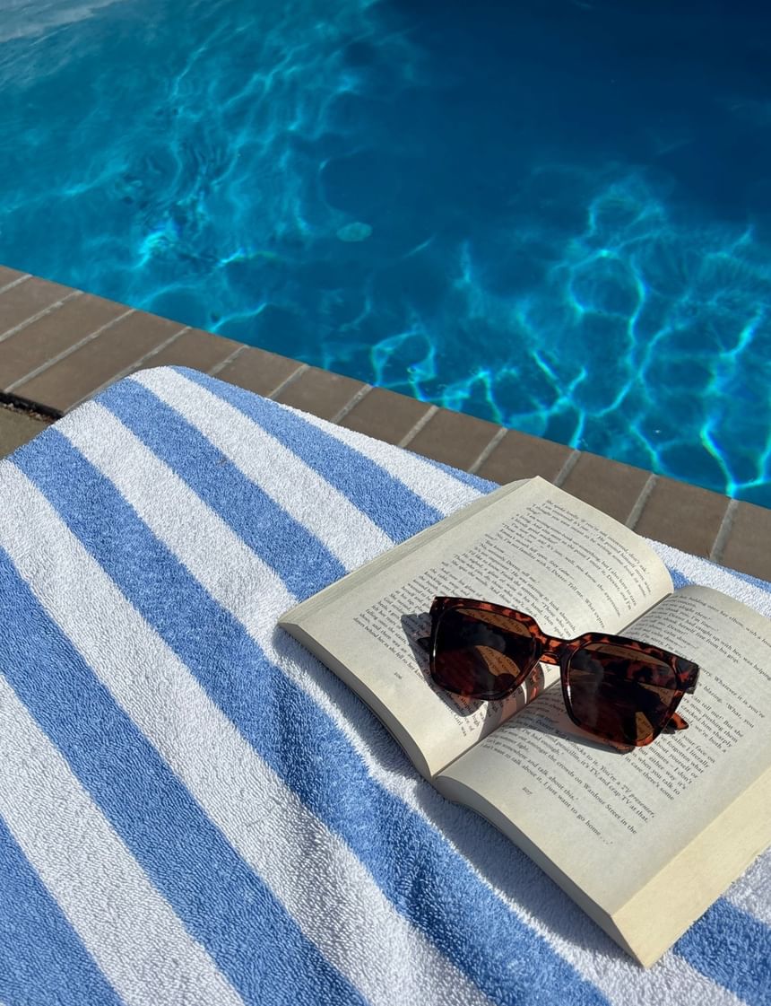 Open book with sunglasses resting on top of a striped towel beside a swimming pool poolside at Avon Old Farms Hotel