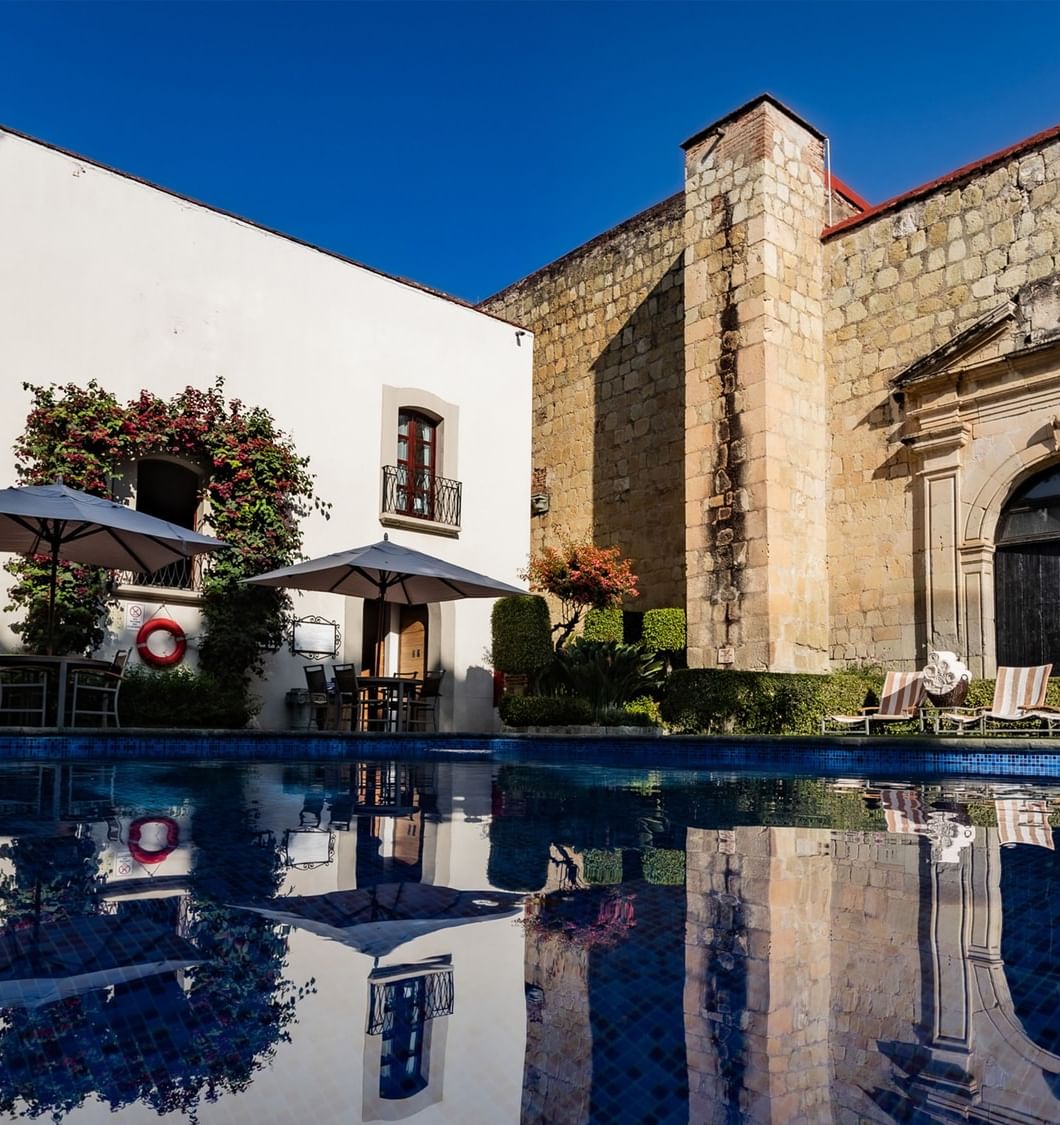 Piscina exterior del hotel reflejando edificios blancos y sombrillas durante el día en Quinta Real Oaxaca