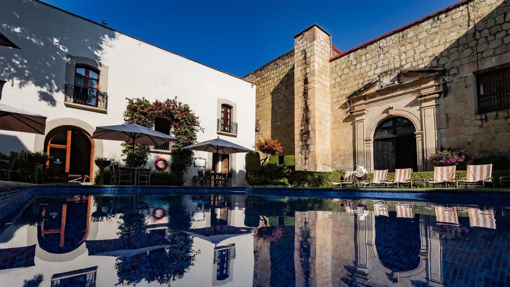Piscina exterior del hotel reflejando edificios blancos y sombrillas durante el día en Quinta Real Oaxaca