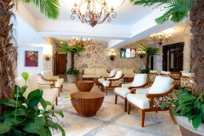 Elegant hotel lobby with white cushioned seating, tropical palms, stone walls, and ornate chandeliers at Playa Los Arcos Puerto Vallarta 2023