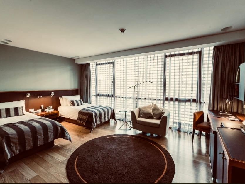 Quarto Deluxe Twin espaçoso com duas camas, piso de madeira, janelas amplas e área de estar no NOI Vitacura