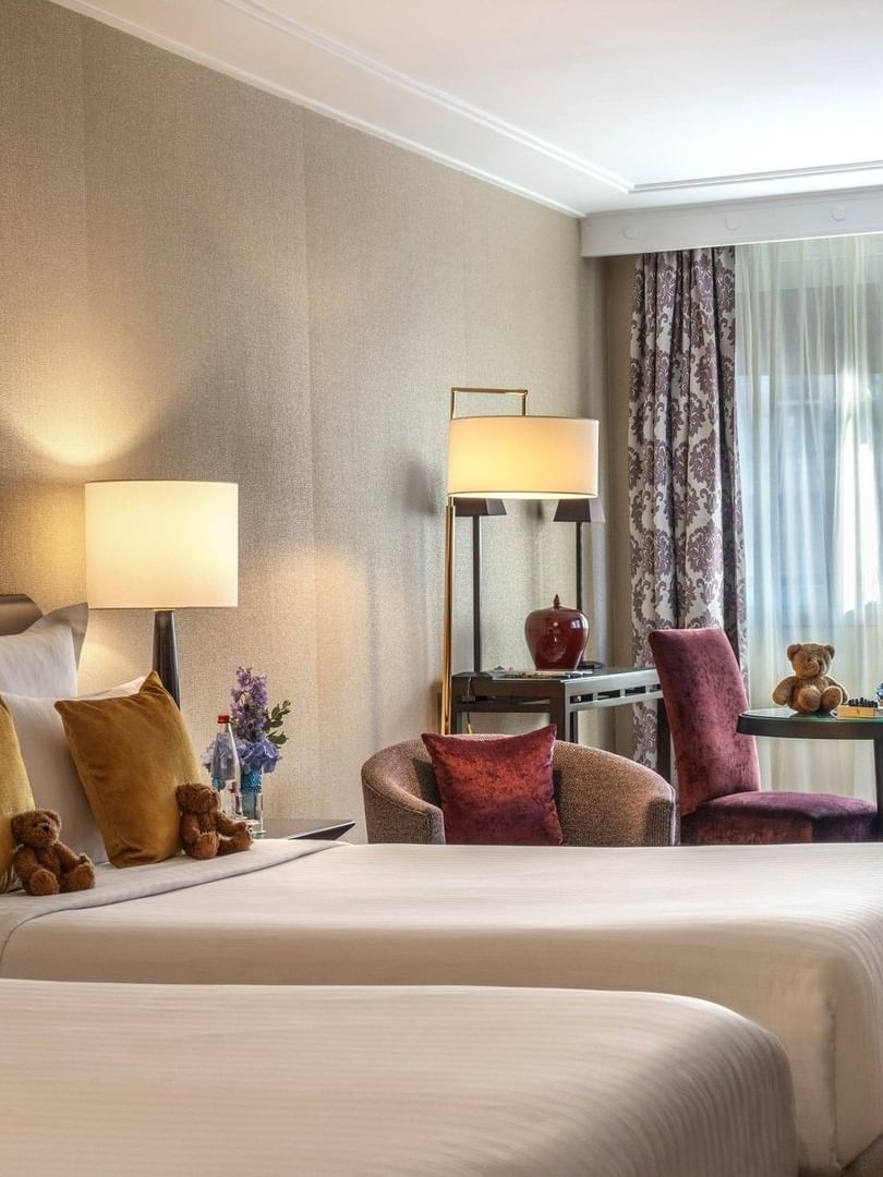 Plush twin beds by a round table with purple chairs in Family room with two queen beds at Warwick Paris Champs Elysées
