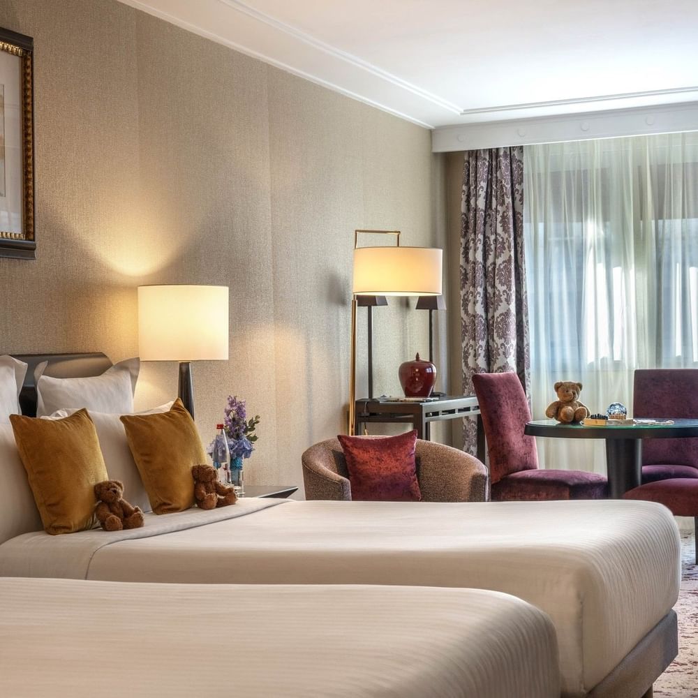 Chambre familiale avec deux lits queen size, un coin salon et des rideaux à l'hôtel Warwick Champs-Élysées à Paris.