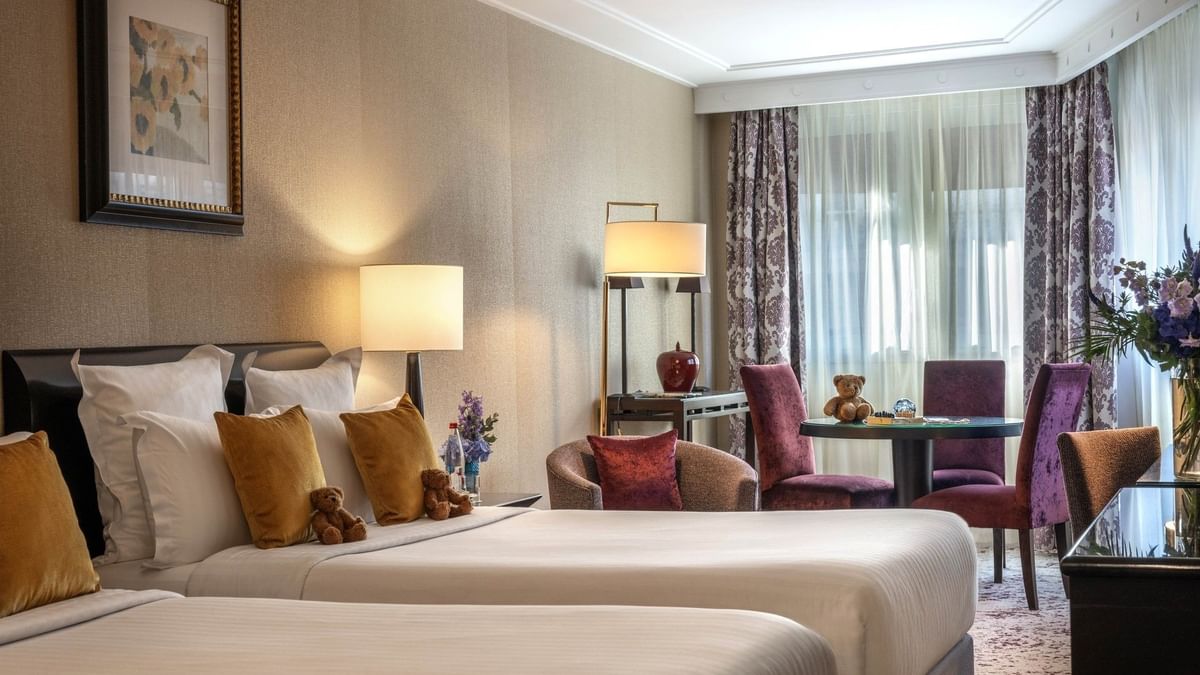 Plush twin beds by a round table with purple chairs in Family room with two queen beds at Warwick Paris Champs Elysées