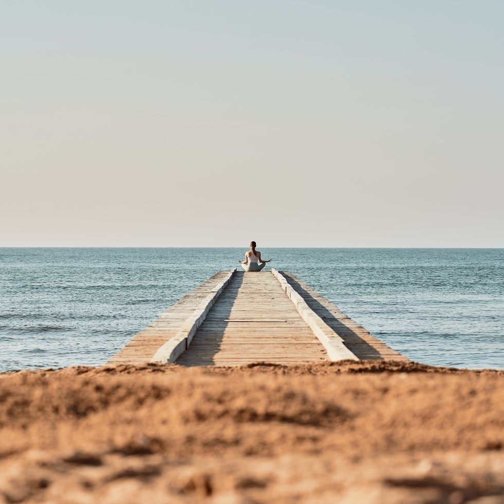 Persona che pratica yoga su una piattaforma in legno sul mare durante il tramonto.